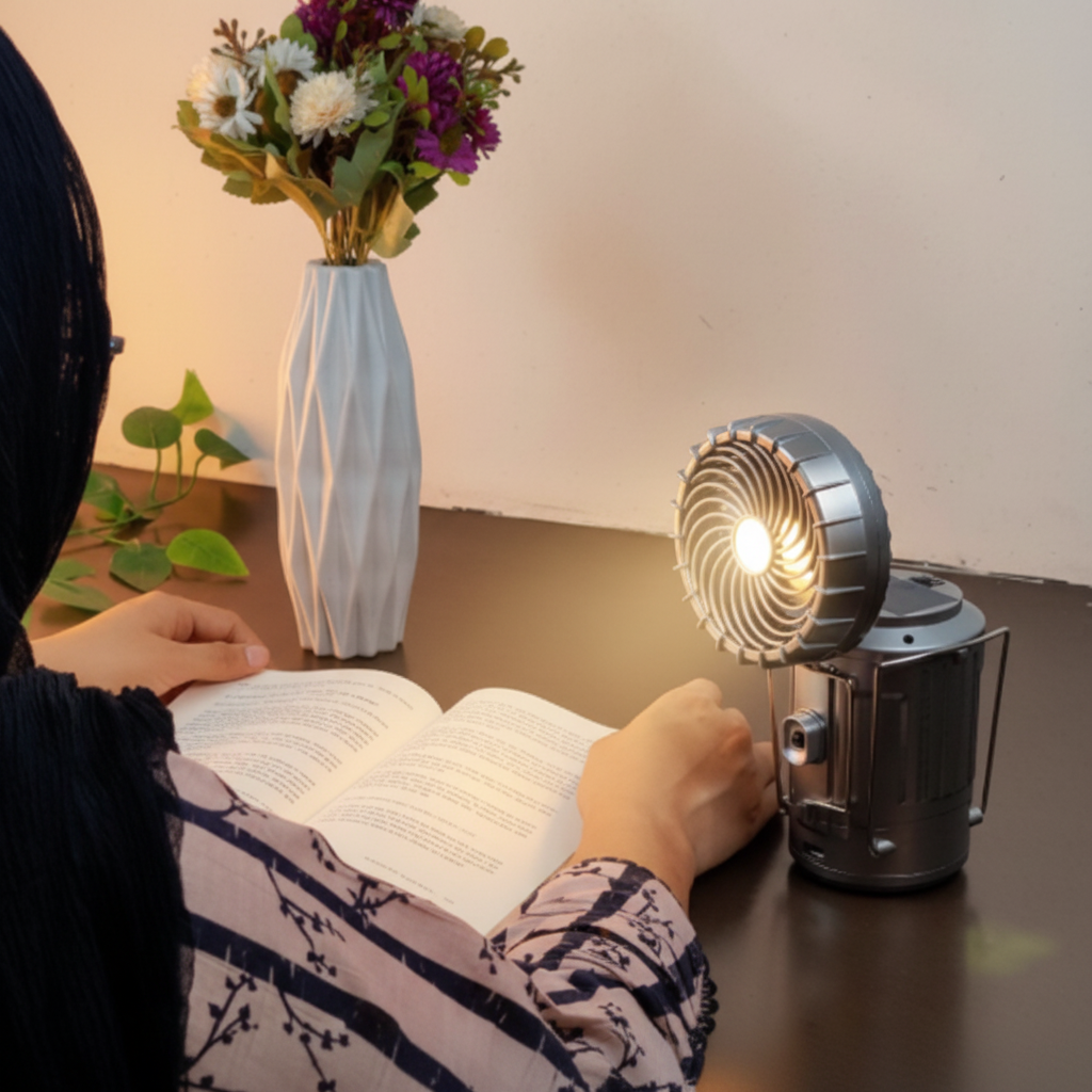Person reading at desk with camping lantern as desktop fan and soft light indoors